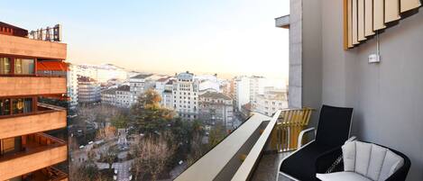 Un balcón con vista a un paisaje urbano, una silla blanco y negro y una pequeña mesa.