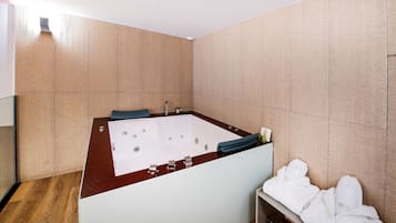 A modern bathroom with a large bathtub, wooden flooring, and a bench with towels.
