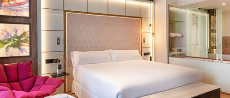 Ein modernes Hotelzimmer mit einem großen Bett, einem Nachttisch mit Lampe, einem roten Sessel und Bildern an der Wand.