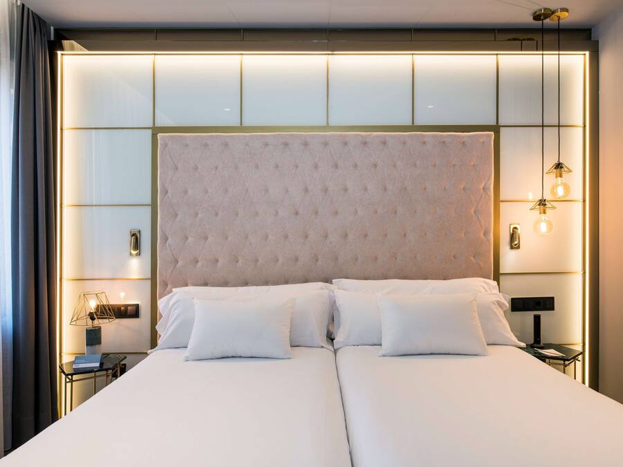 Una cama doble con cabecera acolchada, mesitas de noche con lámparas y una lámpara moderna.