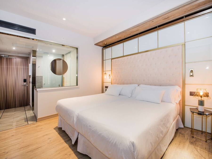 A modern bedroom with a large bed, a bedside table with a lamp, a mirror, and a sliding door leading to another room.