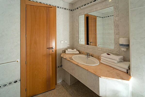 Une salle de bain avec une porte en bois, un lavabo avec un miroir et un distributeur de serviettes.