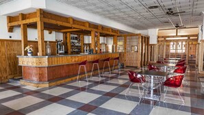 A bar area with a checkered floor, wooden bar counter, and red bar stools. - Hotel Carabela Santa Maria (Moguer)