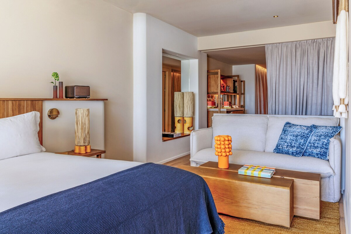 A hotel room with a bed, a sofa, a coffee table, and a small seating area with a lamp.