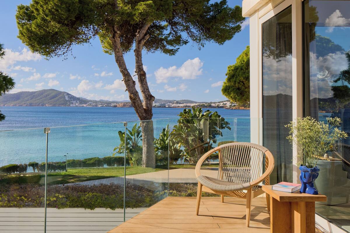 A balcony with a wicker chair, a wooden table, and a vase with flowers.