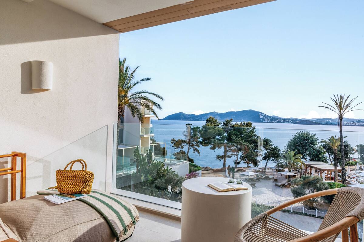 A balcony with a view of the sea, a wicker basket, a book, and a round table.