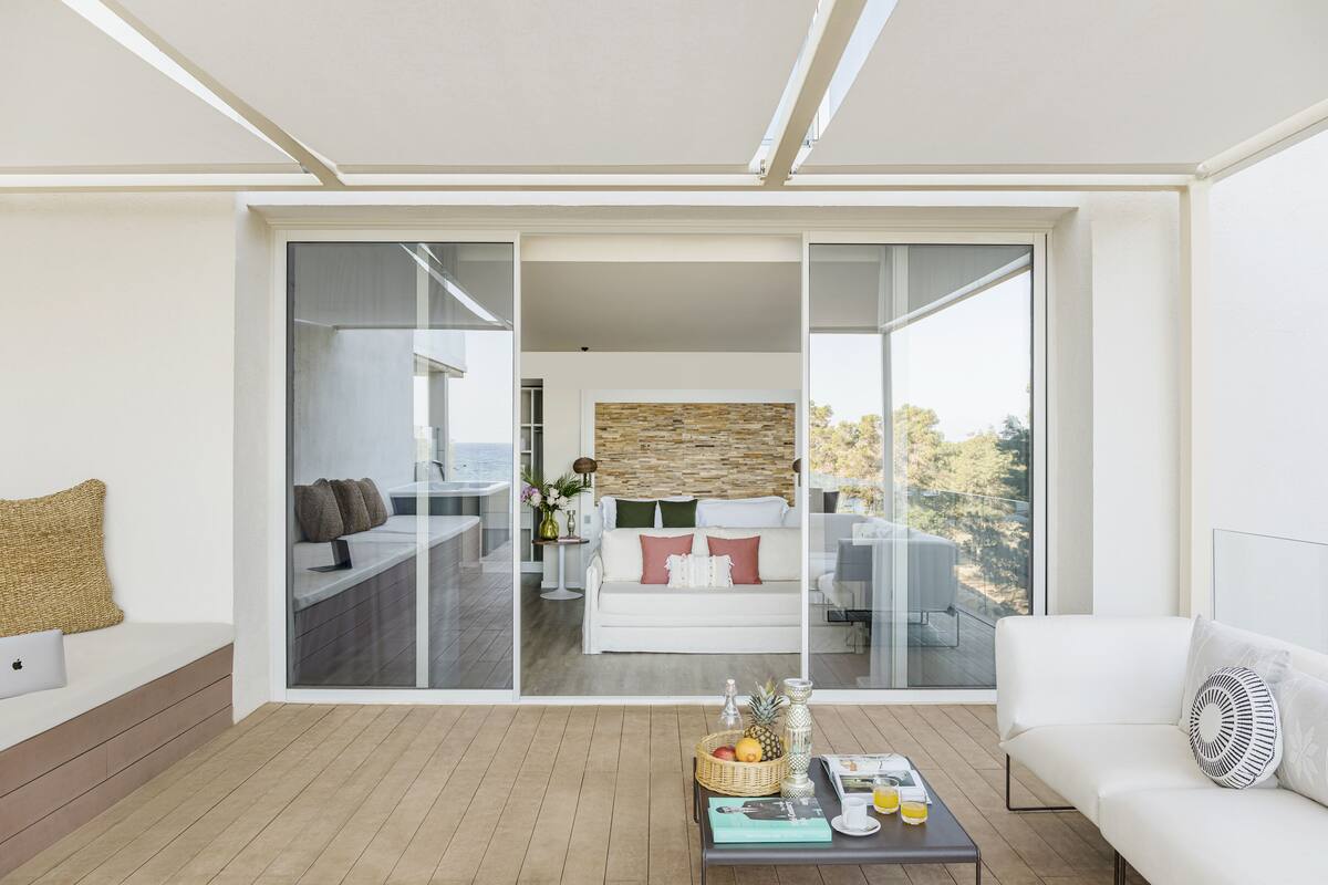 A modern living room with a white sofa, a coffee table with fruits and a book, and a balcony with a white couch and a stone wall.