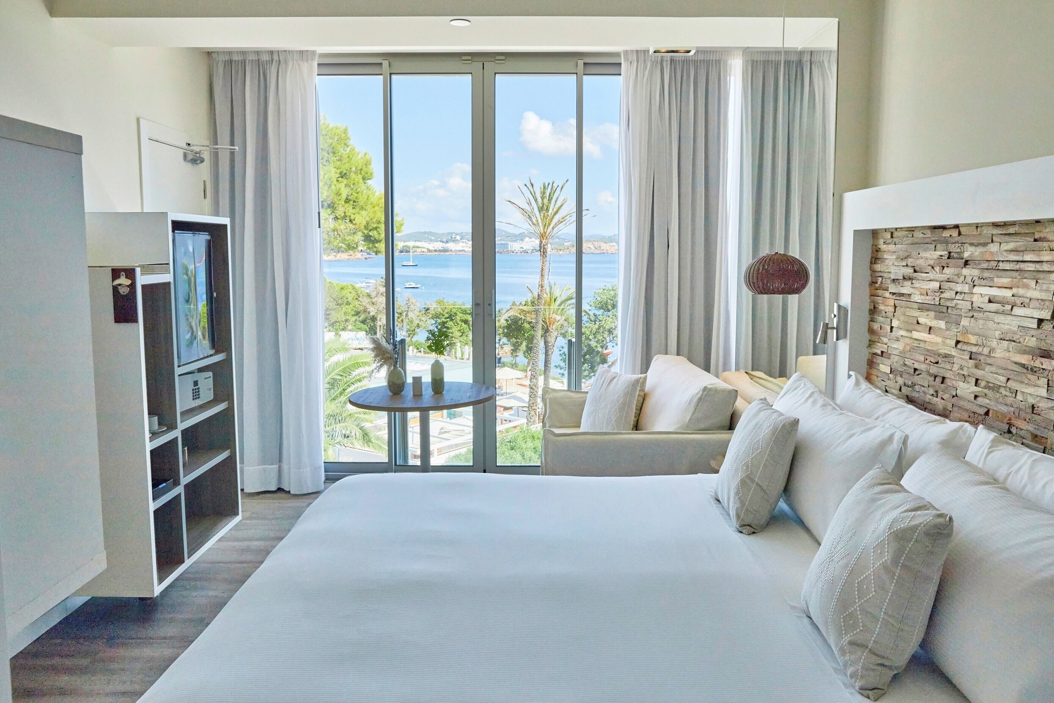 Una camera d'albergo con un letto grande, un divano, una TV e un balcone vista mare.