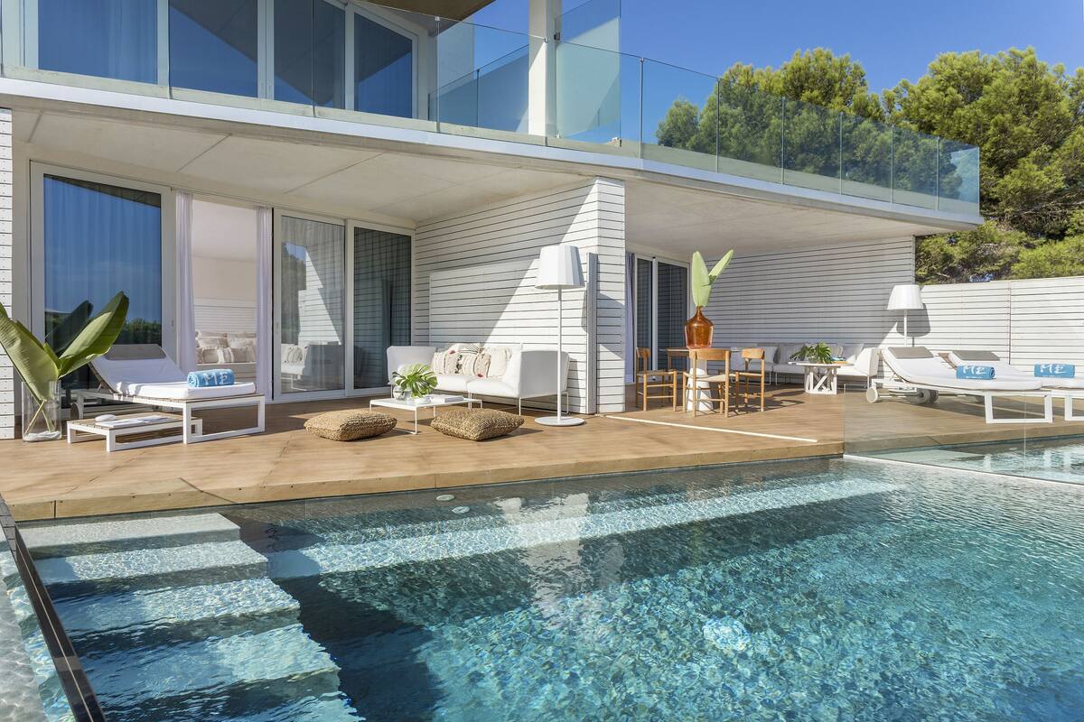 A modern outdoor pool area with a glass balustrade, lounge chairs, and a dining table.
