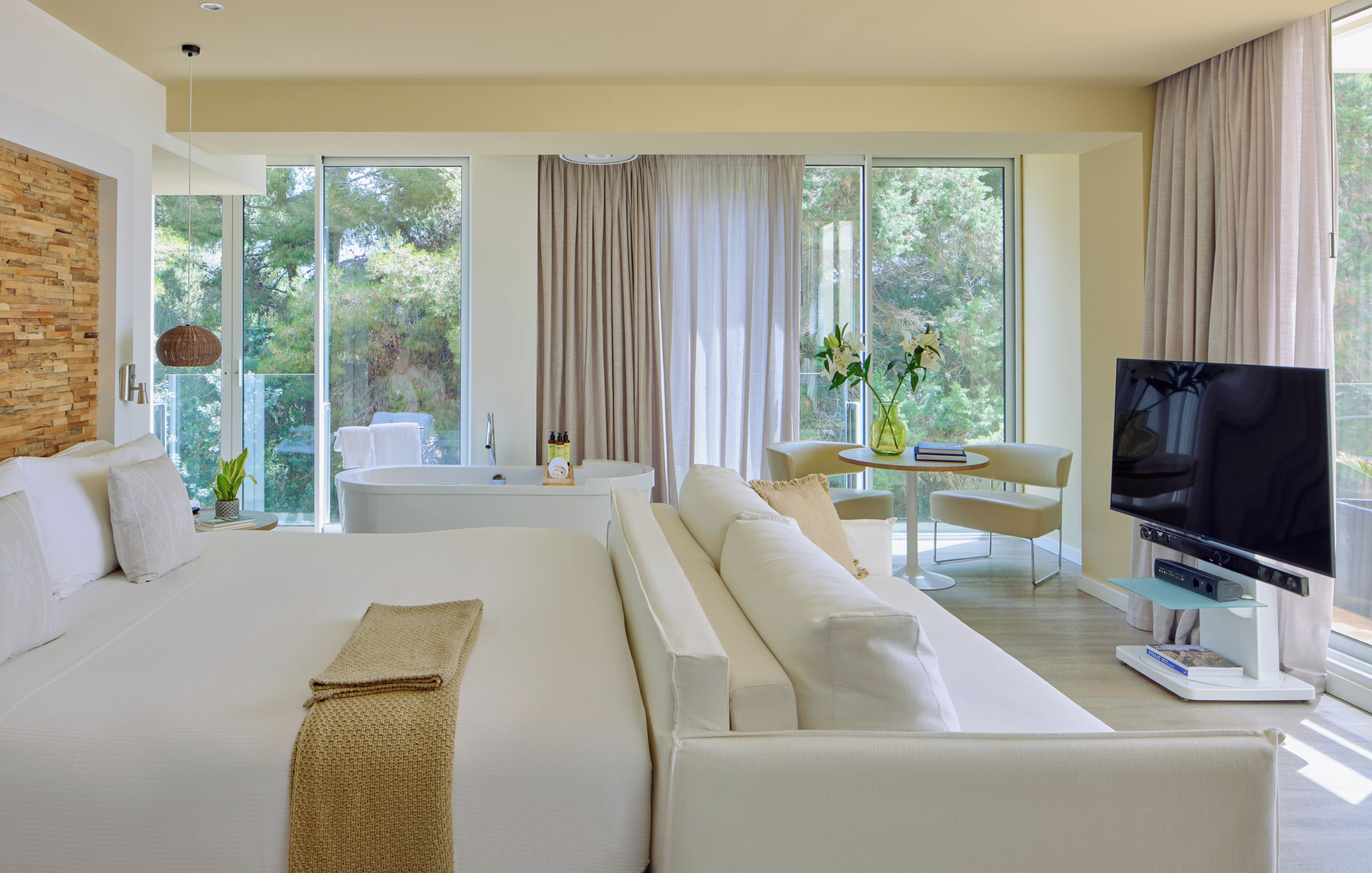 Habitación de hotel moderna con una cama grande, televisión, zona de estar con mesa y vistas al exterior.