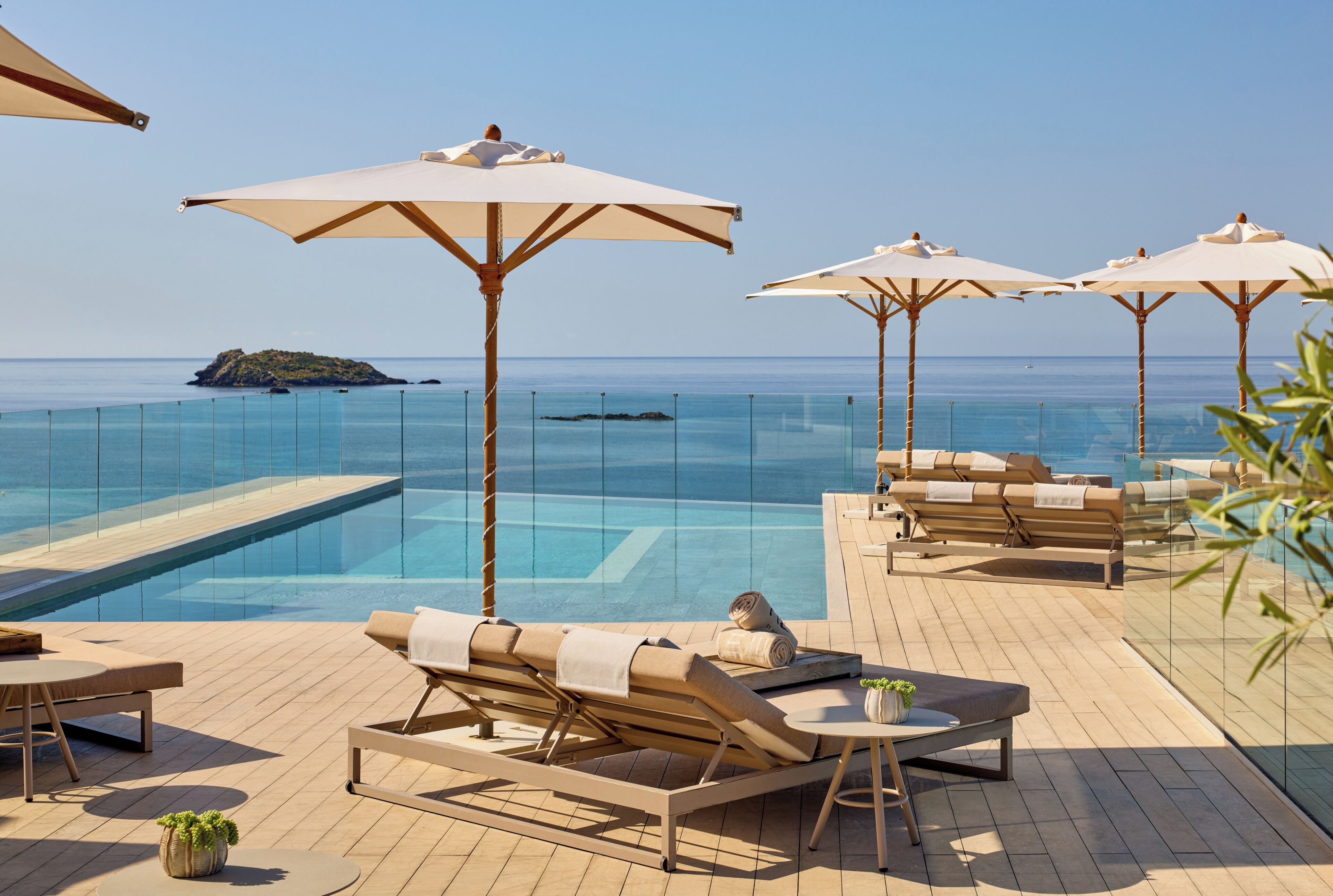 A poolside area with lounge chairs and umbrellas, overlooking a clear blue sea.