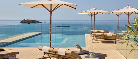 A poolside area with lounge chairs and umbrellas, overlooking a clear blue sea.