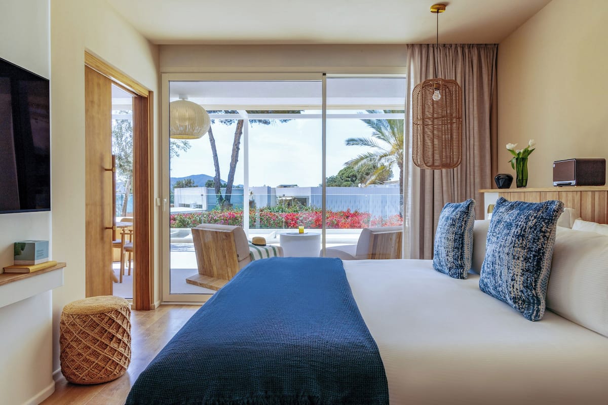 A hotel room with a large bed, a television, a small table, and a view of the outdoors.