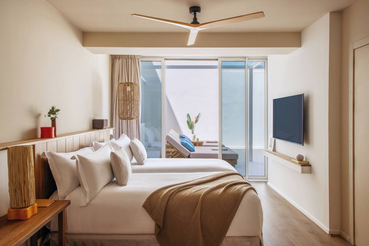 A modern hotel room with a large bed, a ceiling fan, a TV mounted on the wall, and a balcony with a view.