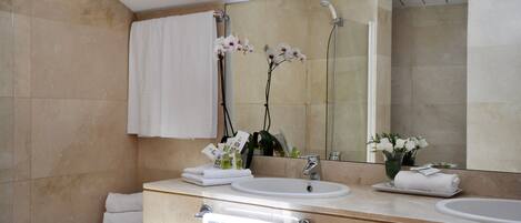 A modern bathroom with a bathtub, two sinks, a large mirror, and decorative orchids.