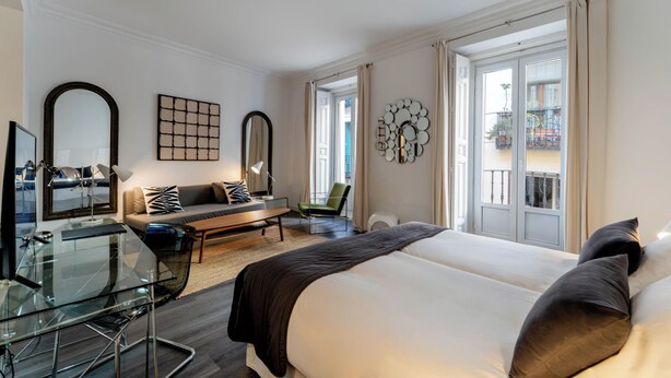 A hotel room with a bed, a desk, a sofa, a chair, and a balcony view. - Suite Prado Hotel (Madrid)