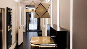 A hotel corridor with a modern interior, a reception desk, and a door leading to the lobby. - Suite Prado Hotel (Madrid)