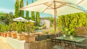 An outdoor patio area with a table and chairs, surrounded by potted plants and umbrellas. - Hotel Costabella (Girona)