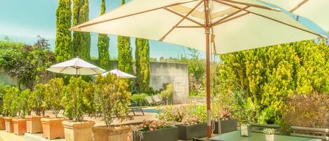 An outdoor patio area with a table and chairs, surrounded by potted plants and umbrellas.
