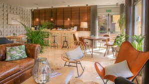 A modern hotel lobby with leather sofas, wicker chairs, and a central bar area. - Hotel Costabella (Girona)