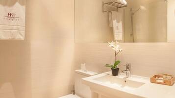 Un baño con un lavabo blanco, un inodoro y un espejo. Hay una toalla colgada en la pared y una planta pequeña sobre el lavabo.