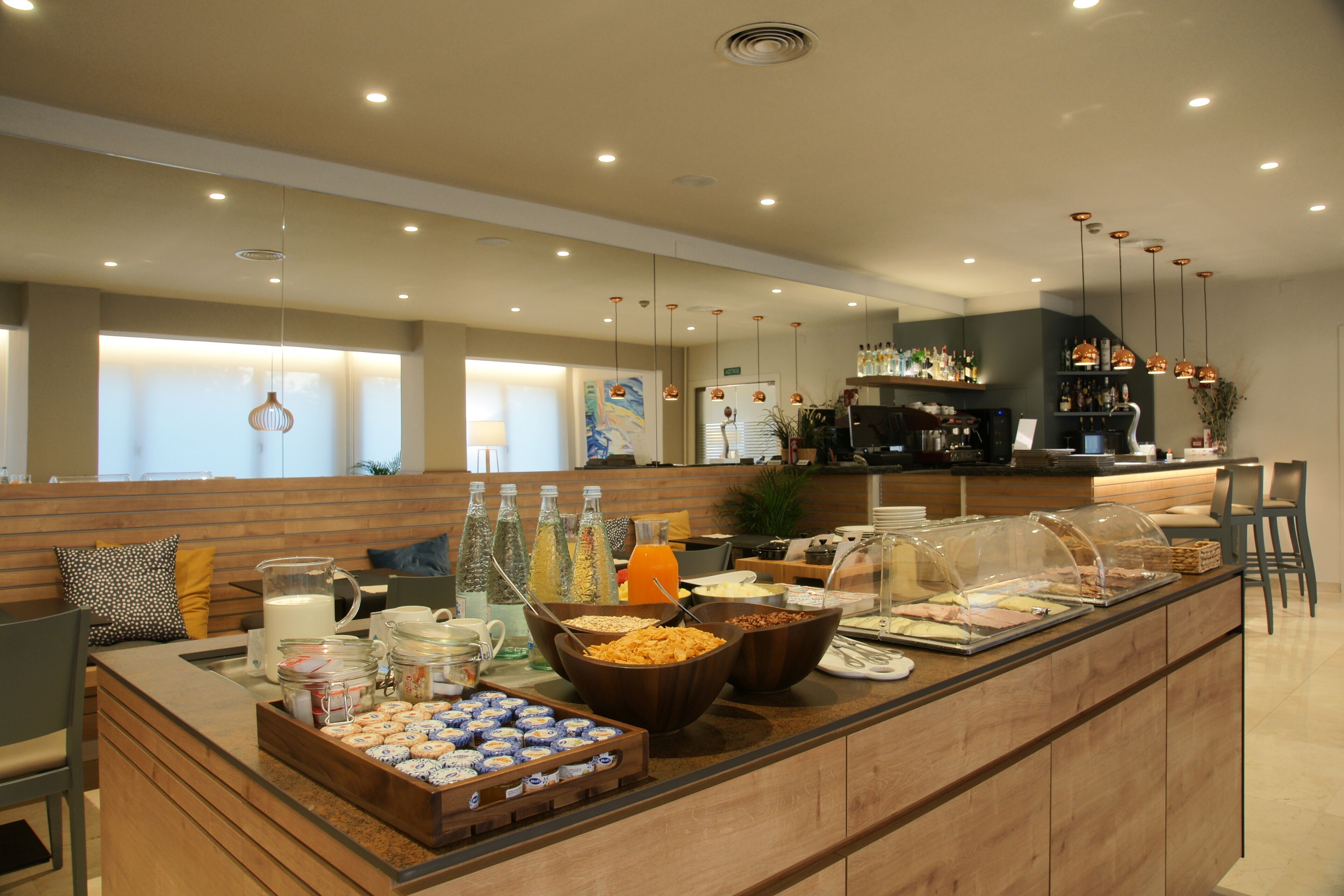 A breakfast buffet with various food items and beverages, a seating area with chairs, and a counter with a coffee machine.