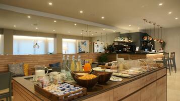 A breakfast buffet with various food items and beverages, a seating area with chairs, and a counter with a coffee machine.