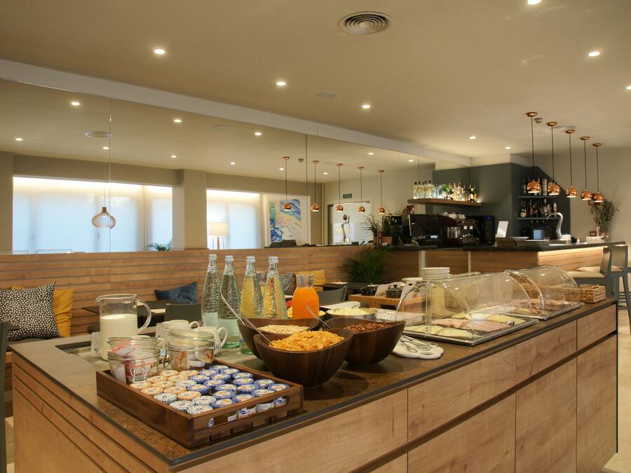 A breakfast buffet with various food items and beverages, a seating area with chairs, and a counter with a coffee machine.