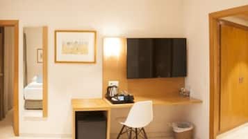A hotel room with a desk, a chair, a television mounted on the wall, a framed picture, and a wooden door.