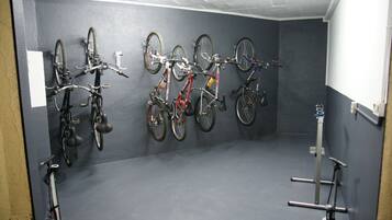 Quarto com piso e paredes cinzas, contendo um suporte com várias bicicletas.