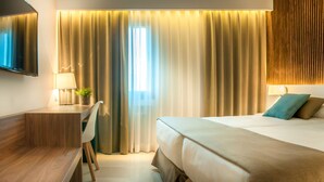 A hotel room with a bed, bedside tables, a TV, curtains, and a wooden panel wall. - Hotel Costabella (Girona)