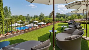 A poolside area with outdoor seating and umbrellas, surrounded by greenery and a view of a pool. - Hotel Costabella (Girona)
