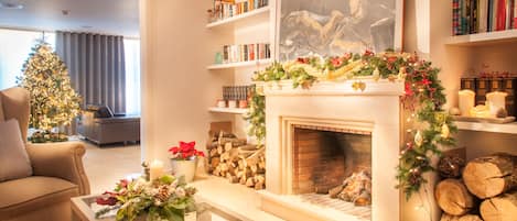 A cozy living room with a fireplace, a Christmas tree, and a bookshelf filled with books.