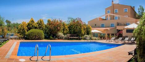 A swimming pool with a clear blue water, surrounded by lounge chairs and a building with a balcony.