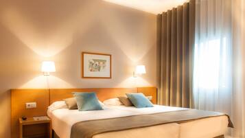 Una habitación de hotel con una cama grande, dos lámparas de noche, un cuadro enmarcado en la pared y una ventana con cortinas.