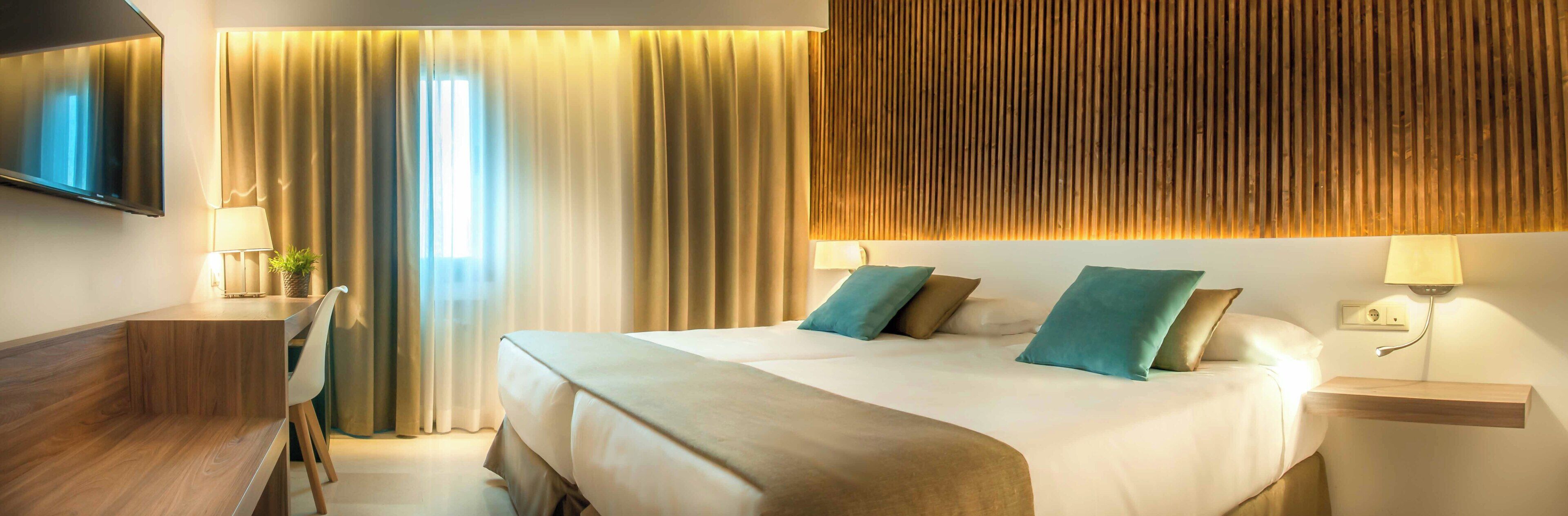 A hotel room with a bed, bedside tables, a TV, and curtains.