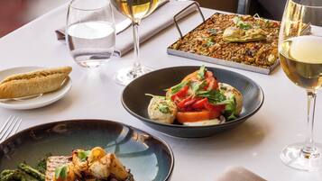 Una mesa de comedor con diversos platos, copas de vino blanco y una servilleta doblada con un tenedor y cuchillo de plata.