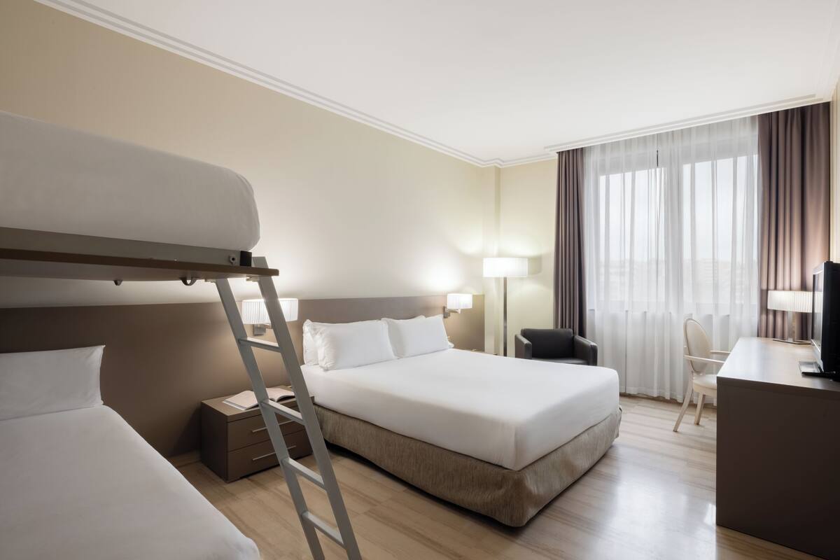 Een hotelkamer met een stapelbed, een bureau, een stoel, een lamp en een televisie.