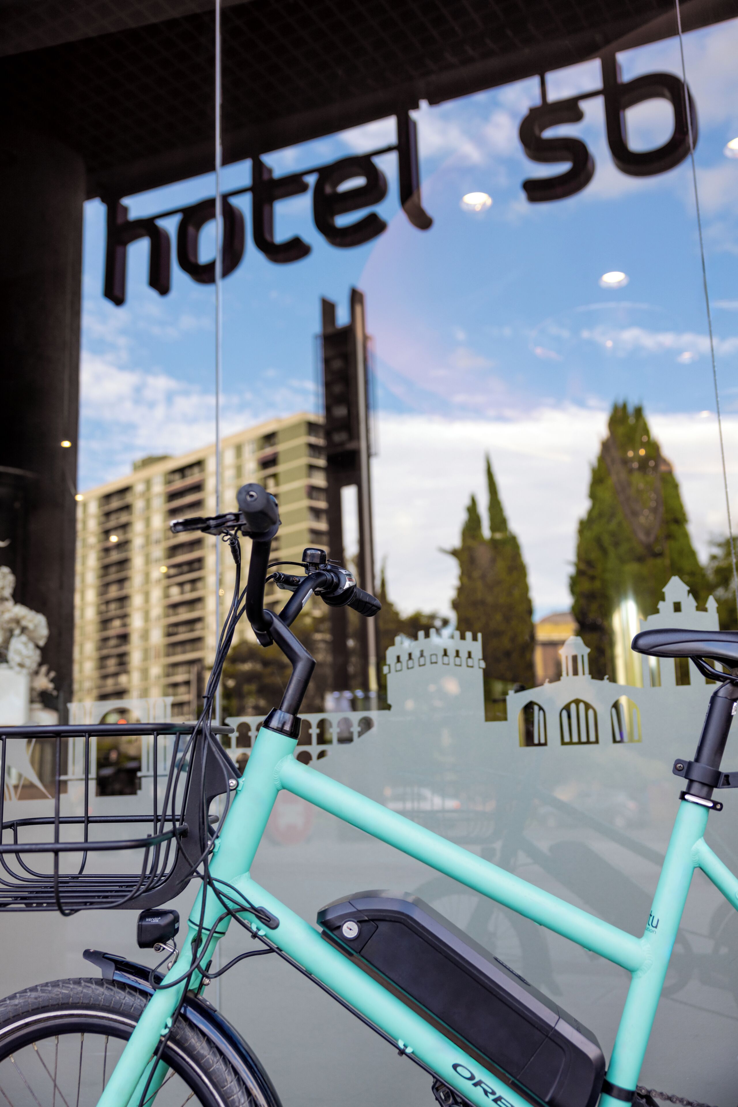 Una bicicleta color turquesa estacionada frente a un edificio con un letrero que dice 'hotel sb'.