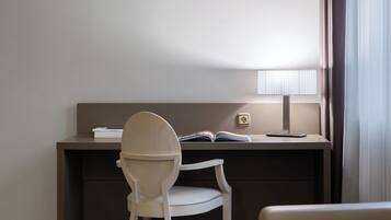 A modern hotel room with a desk, chair, lamp, and a view of the outdoors.