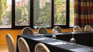 Ein Konferenzraum mit Tisch für eine Besprechung, großen Fenstern mit Blick auf Bäume und Gebäude sowie einem Karomuster-Vorhang.