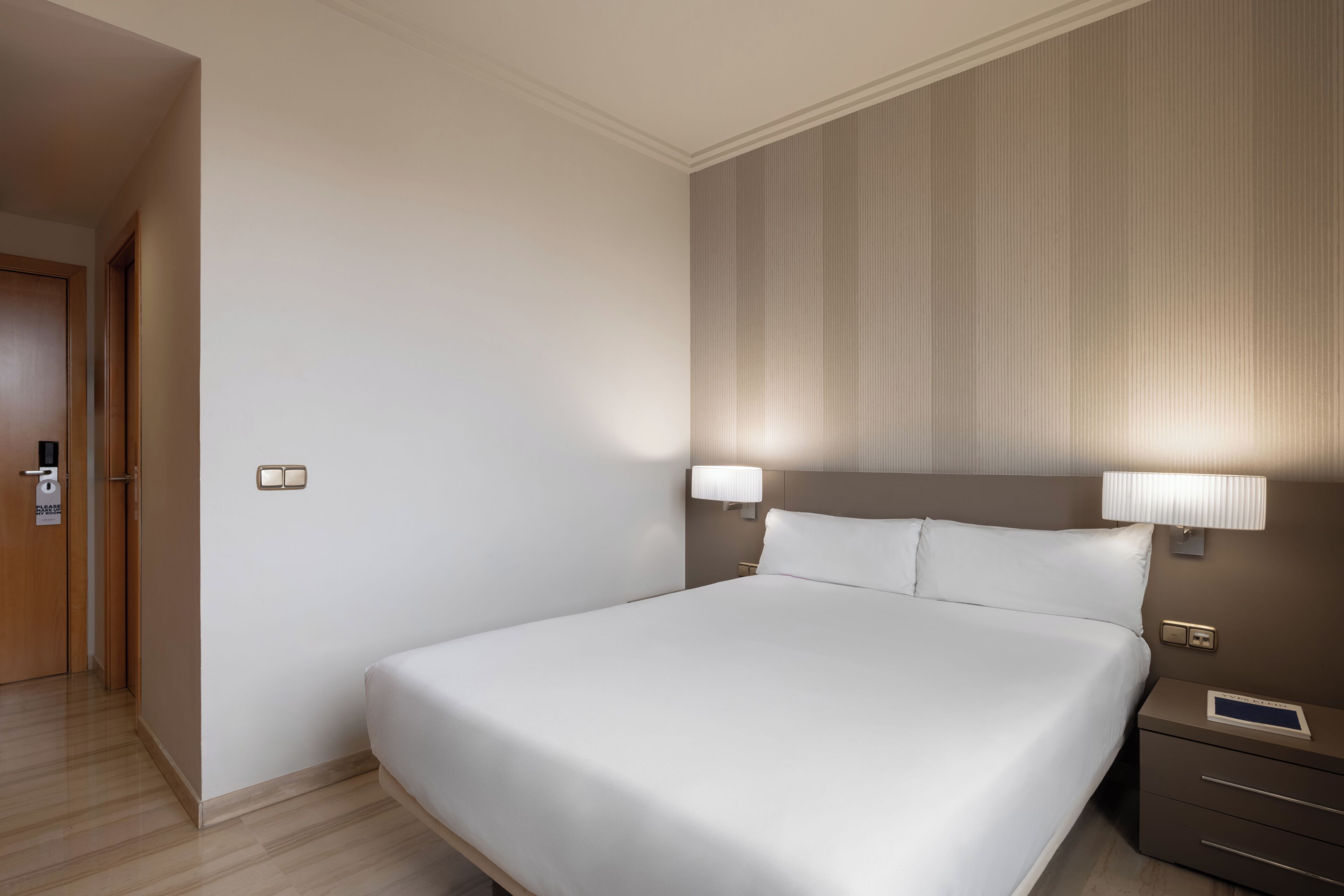 A hotel room with a large bed, bedside lamps, a nightstand, and a door.