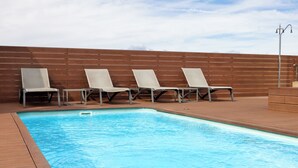 Ein Schwimmbecken mit vier Liegestühlen und einer Holzterrasse.
