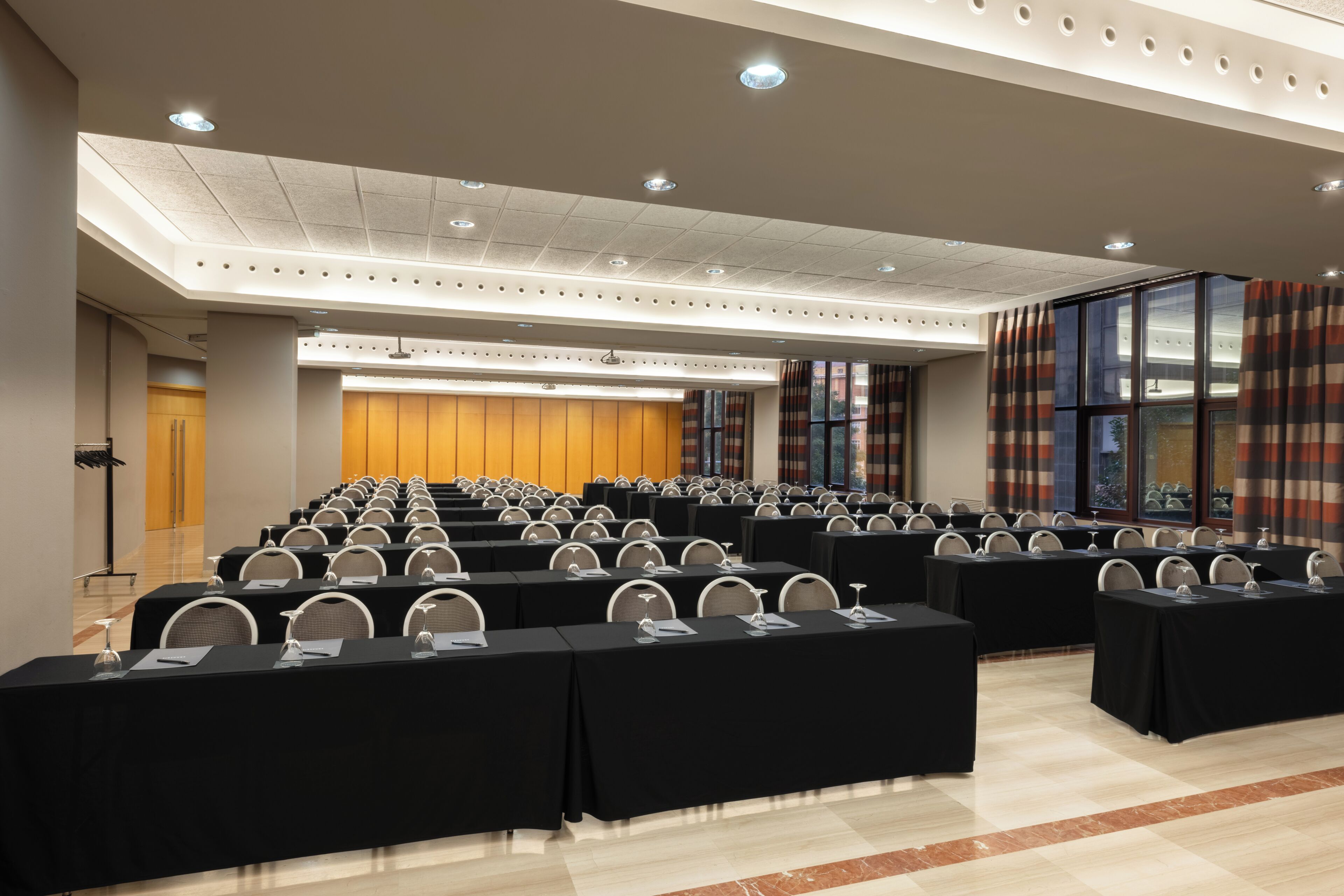 A conference room with rows of tables and chairs, a podium, and a large window with curtains.