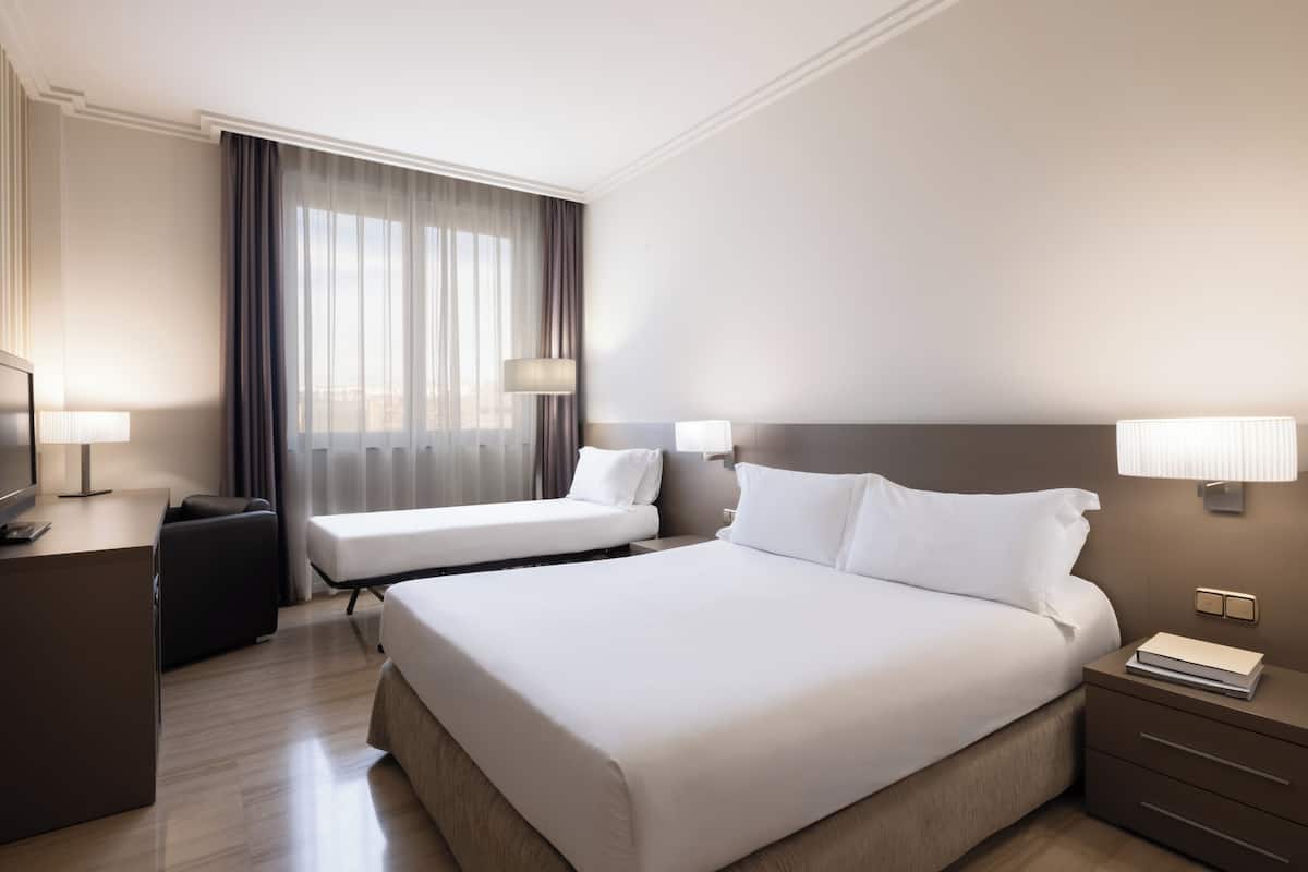Habitación de hotel con una cama grande, dos mesitas de noche, un escritorio con lámpara y televisión.