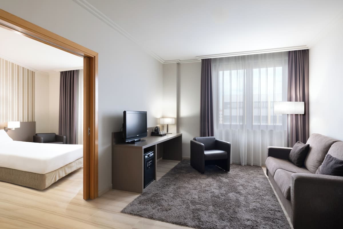 Een hotelkamer met een bed, een bureau met een televisie, een bank en een groot raam met gordijnen.