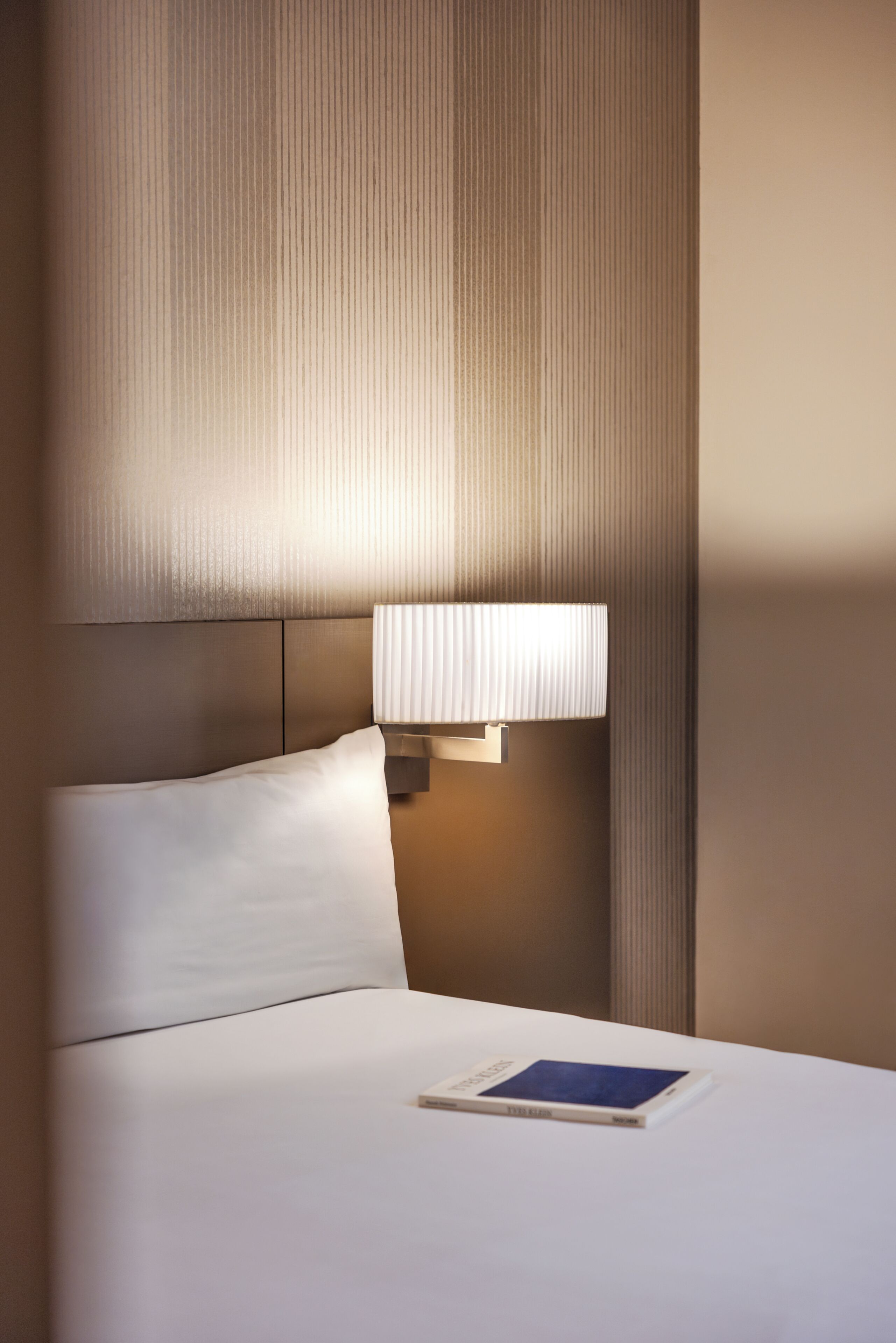 Una habitación de hotel con una cama, una mesita de noche, una lámpara y un libro sobre la cama.