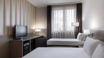 Une chambre d’hôtel équipée d’un téléviseur à écran plat, d’un bureau avec une lampe, de deux lits et d’une grande fenêtre avec des rideaux.