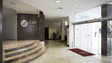 A hotel lobby with marble flooring, a staircase leading to the upper level, and a reception desk.