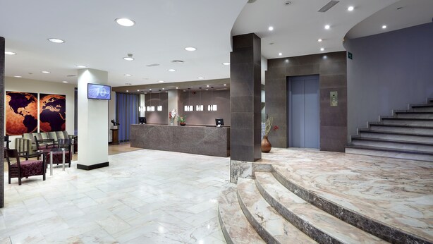 A hotel lobby with a reception desk, seating area, and marble flooring. - Hotel Dorma Tartessos (Huelva)